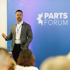 A man is standing in front of an audience. The background is purple and faded, it includes the PARTS FORUM logo in white. The man is called Stephen Fauth and is Co-CEO of MARKT-PILOT.